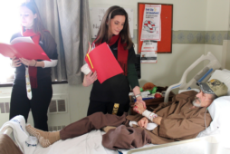 Veteran Joe Hughson holds the hand of a VA Acquisition Academy intern as he listens to carols during Operation Holiday Cheer, an intern mission service project, at the Martinsburg VA Medical Center